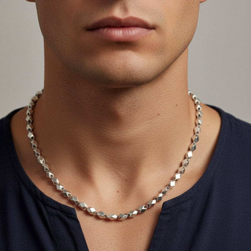 Man wearing a silver chain necklace against a neutral background