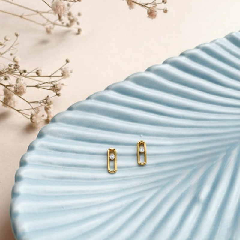 Gold earrings on a textured blue surface with dried flowers in the background